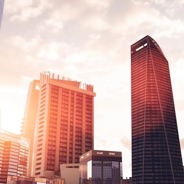 Modern city skyline with glass office towers and high-rise buildings illuminated by warm sunlight.