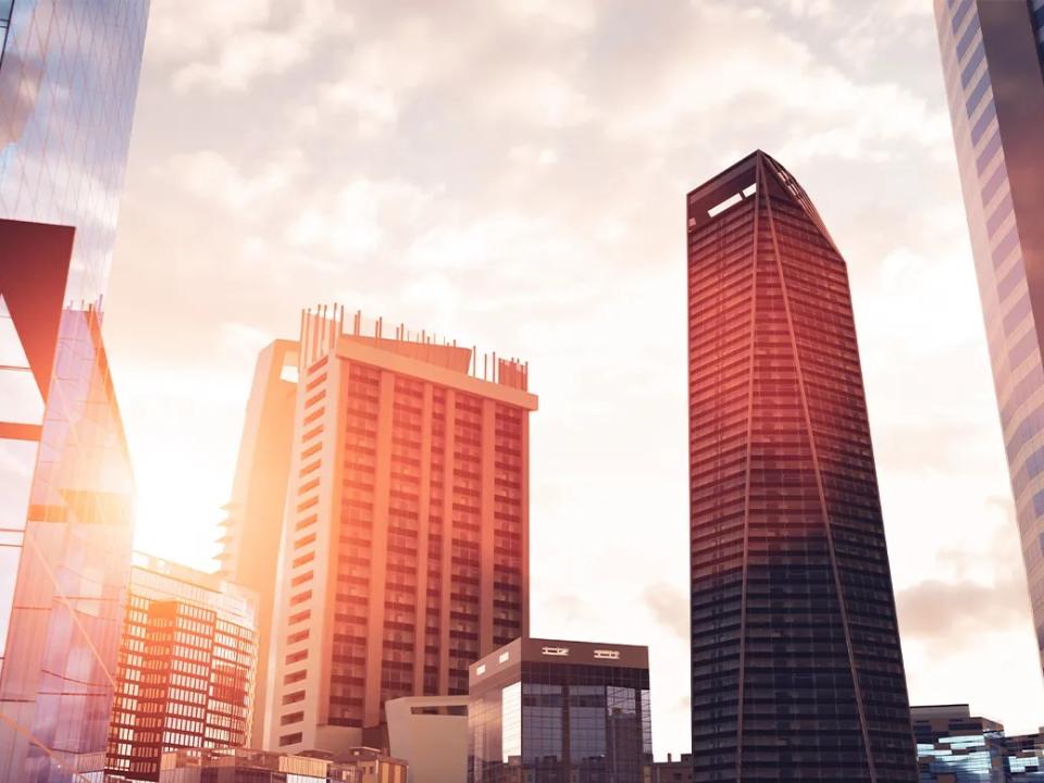 Modern city skyline with glass office towers and high-rise buildings illuminated by warm sunlight.