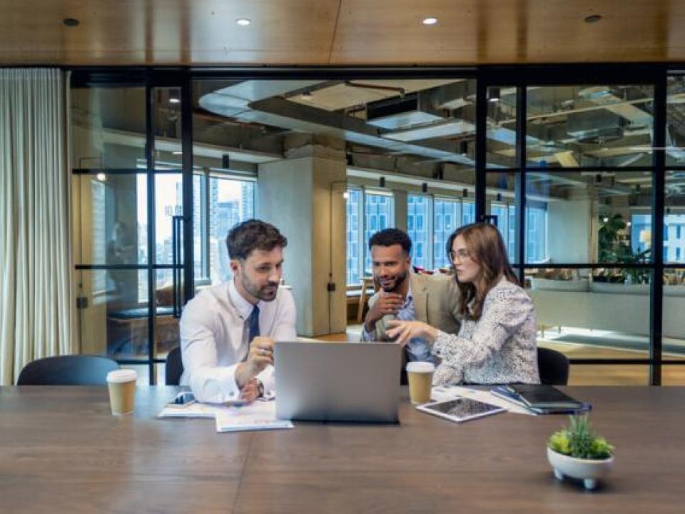 Three colleagues sitting at a table looking at laptop screen