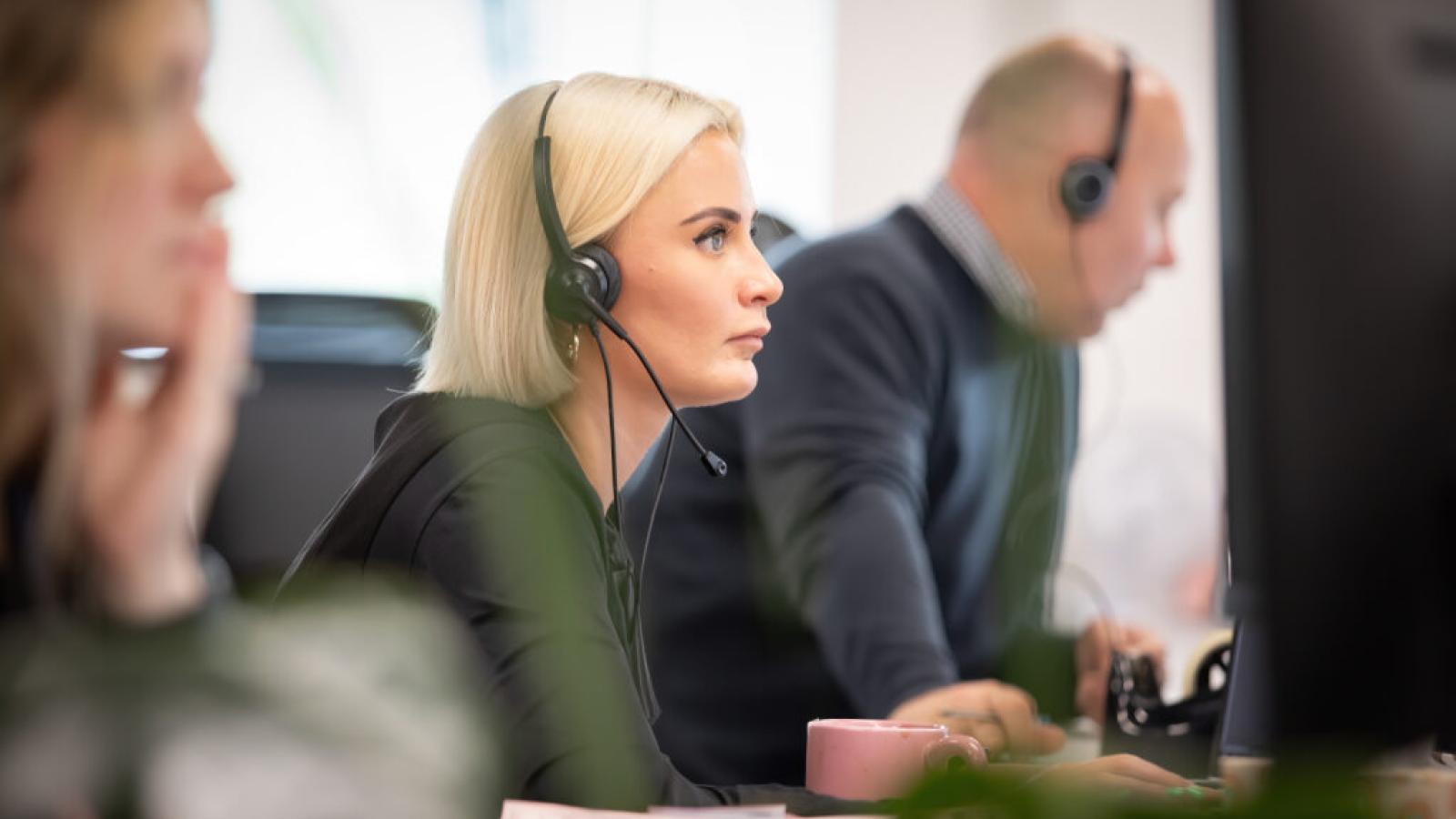 Team members working at computer stations wearing headsets in an office environment